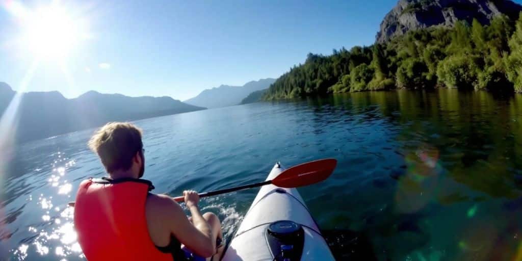 Person kayaking on a lake with mountains in background.