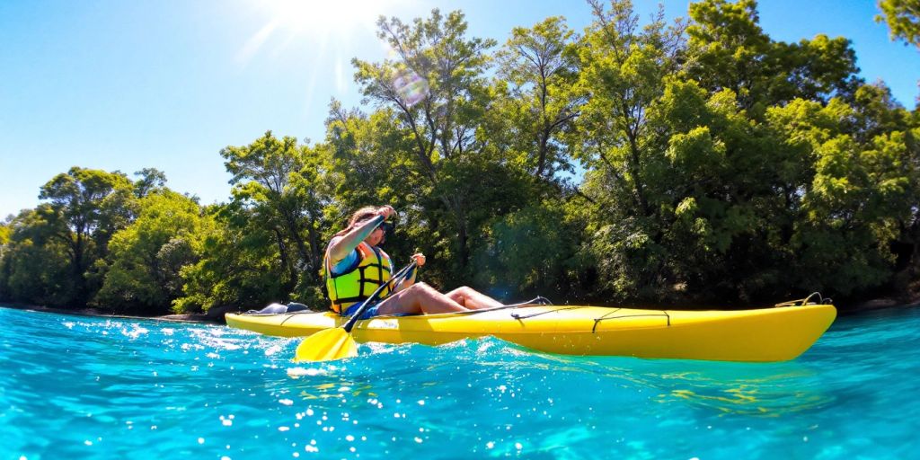 Kayaker paddling through blue water in a lush setting.